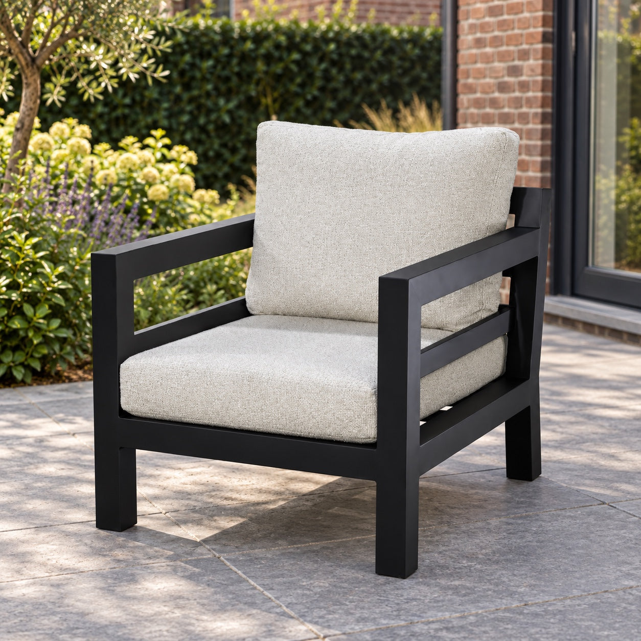Yoi Midori loungestoel met zwart frame en lichte kussens in een Nederlandse achtertuin.
