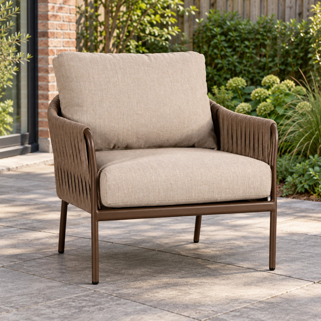 Yoi Hydra loungestoel in bronze en toffee met beige kussens op een terras.