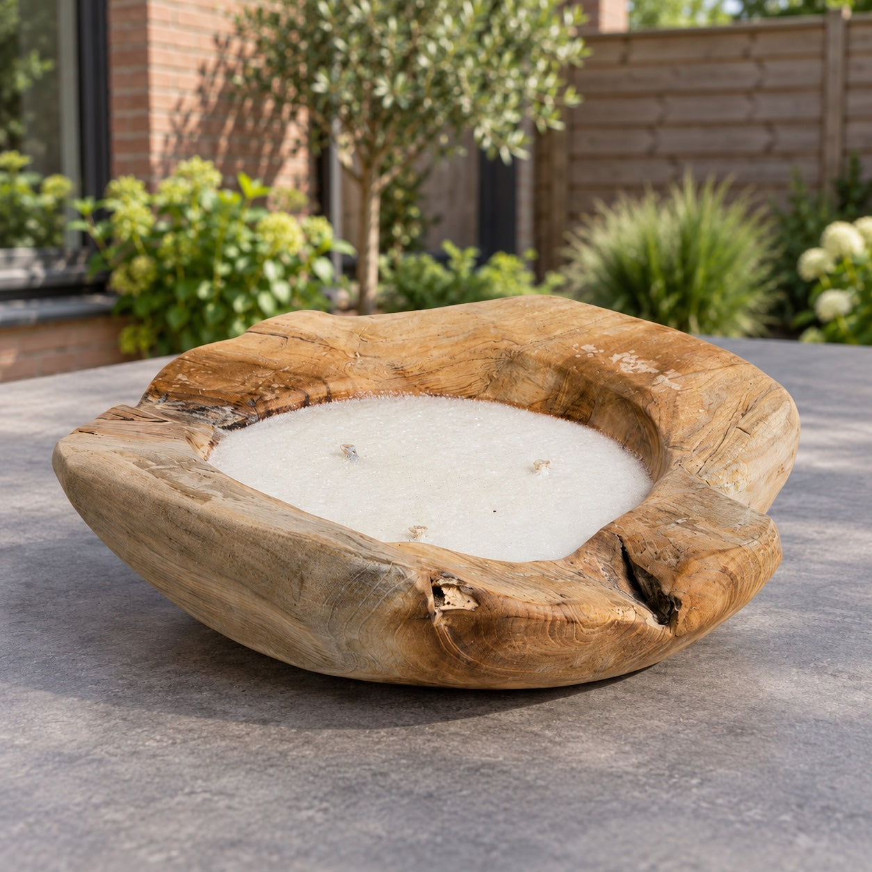 Tierra Outdoor teakhouten kaarsenschaal met drie lonten op een tuintafel.